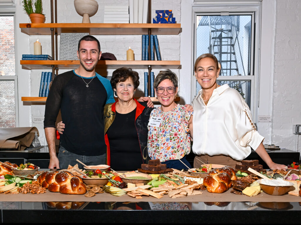 Four people are standing in front of a grazing table, smiling with their arms around one another.